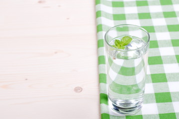 glass of clean water with mint on a table covered with a checker