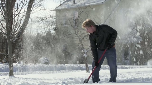 Teenager shovels snow quickly in the Mid West, USA.  Full length shot from side with camera movement.