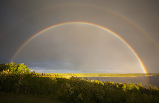 A double rainbow in the sky arching over the land. 