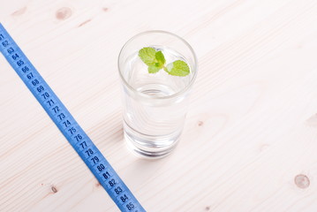 glass of clean water with mint on a table next to a centimeter d