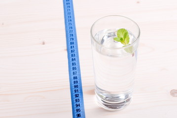 glass of clean water with mint on a table next to a centimeter d