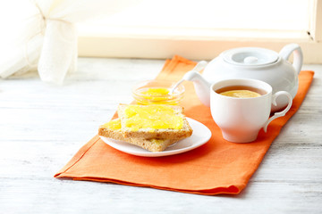 Toasts with honey on plate and cup of tea on light background