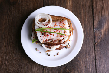 Sandwiches with lard and onion on plate on wooden background
