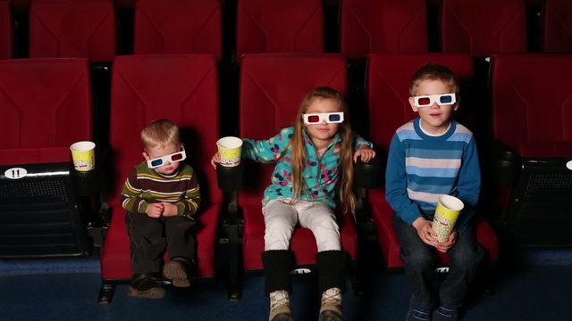 Girl and two boys with popcorn watching 3D film in the cinema