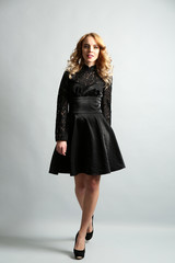 Beautiful young woman in black dress posing on light background