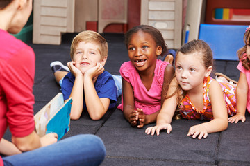 Lachende Kinder im Kindergarten hören zu - obrazy, fototapety, plakaty