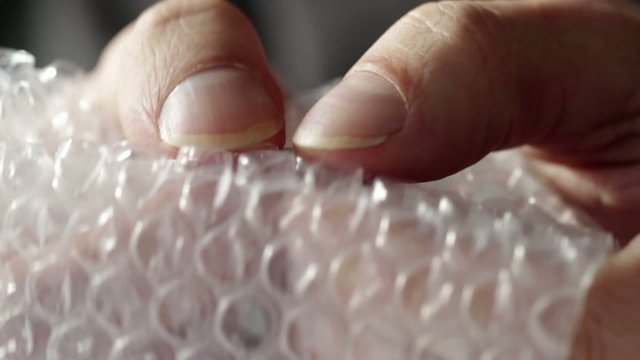 Fingers bursting air pockets in a sheet of transparent bubble wrap.  Two clips recorded with macro lens and shallow depth of field.