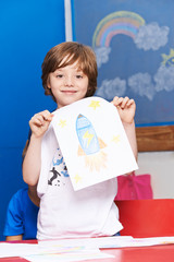 Kind zeigt stolz Rakete auf Blatt Papier