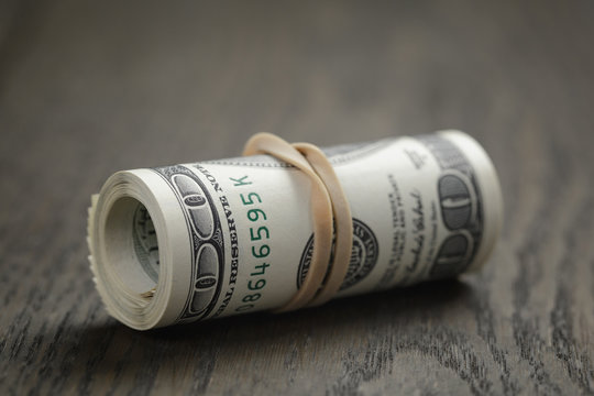 Roll Of Hundred Dollar Bills On Wooden Table