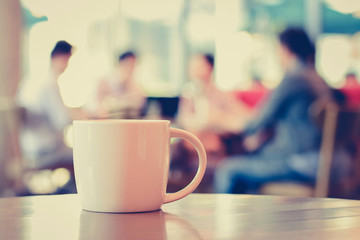 Coffee cup on the table with people in coffee shop -vintage tone