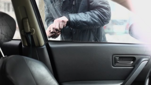 Man in leather jacket tries to break door lock of car