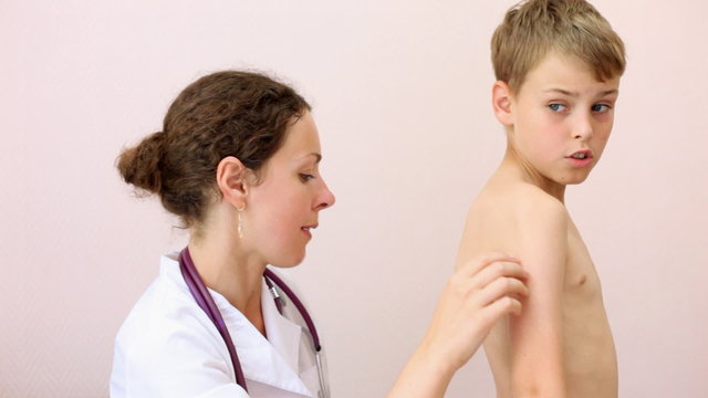 woman doctor in white dressing inspection back of boy in policlinic office