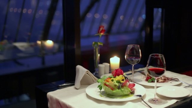 Candle burns on table with glasses of wine and meals at dishes