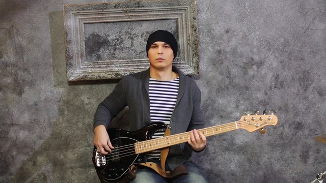 Young man in striped vest and knitted jacket sits with guitar 