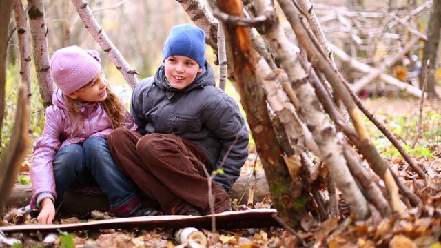 Boy and girl sit in hut made of thin birch trunks at autumn park