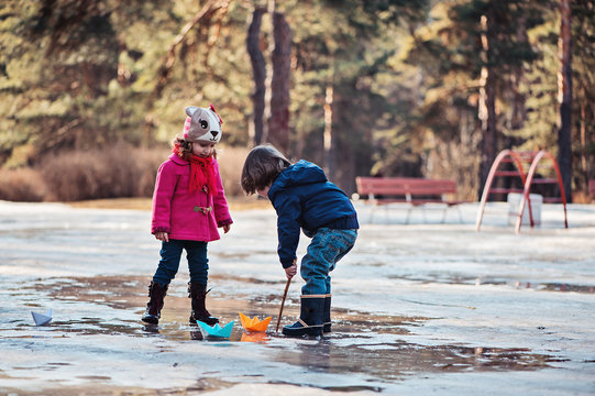 boy and girl playing in spring puddle with paper boats