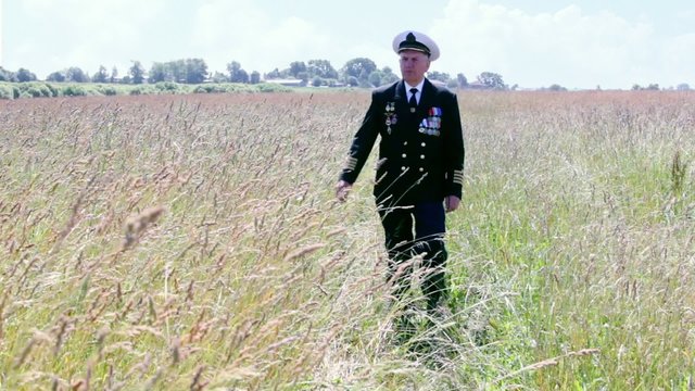 Old man in marine uniform approach among grass in field