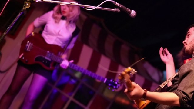 Young man and woman play on guitars on stage during concert