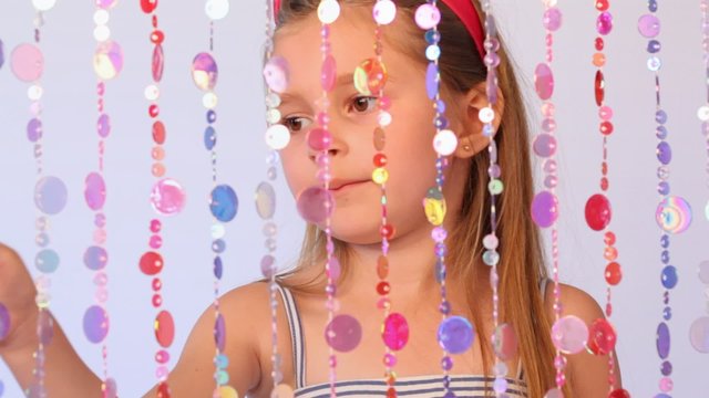 girl behind curtain from threads with multi-colored round plates counts them showing on everyone finger