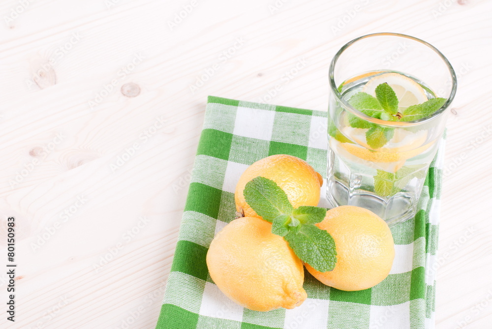 Wall mural water with lemon and mint in a glass on the table top viewew