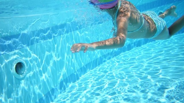 Little girl swimming under water in the pool in swimming glasses