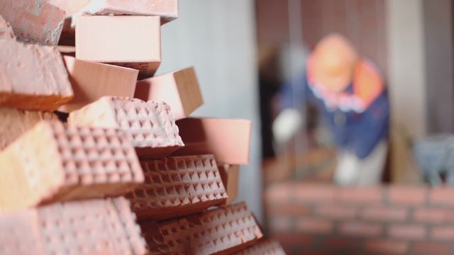 Pile of bricks at background of few workers build wall unfocused