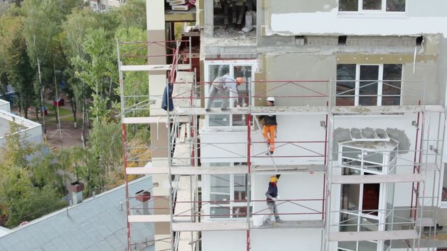 Workers stand on falsework and make thermoinsulation of wall