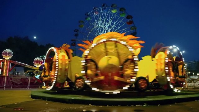 People ride on rotary attraction Kolobok and Ferris wheel