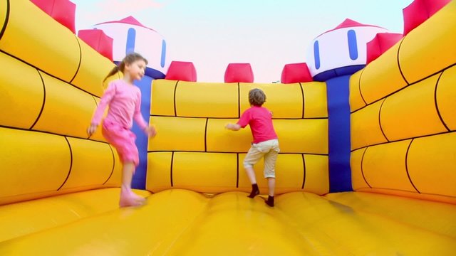 Pair of children boy and little girl jump at inflatable playground at sunny summer day