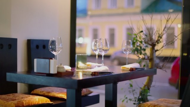 Evening street traffic behind window of restaurant where candle burns at table with glasses and chopsticks, shown in motion