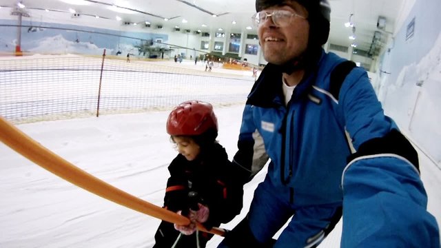 Father with daughter rise on skilift in ski complex