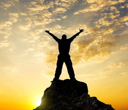 Silhouette of the person standing on a rock in beams of a declin