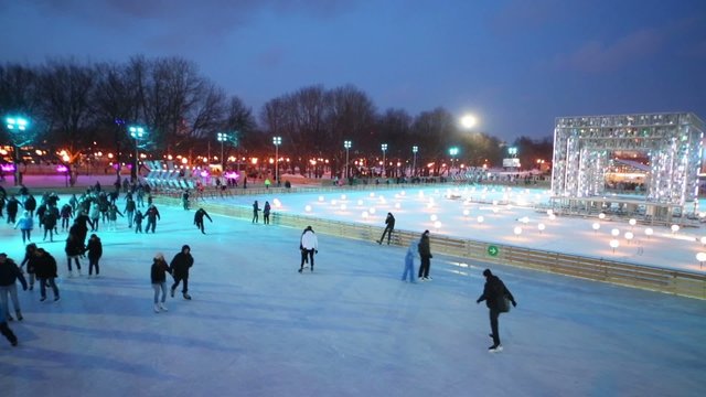 People are skating on evening rink with lampposts 