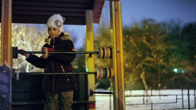 Little girl in warm clothes plays on playground at winter