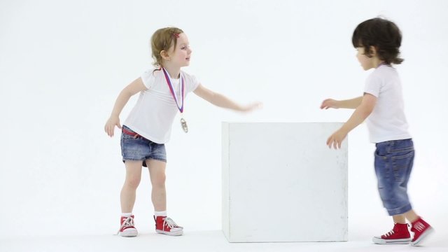 Little girl and boy in shorts with medal plays with big cube