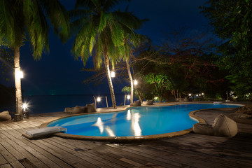 Fototapeta na wymiar Swimming pool with palms on beach at night