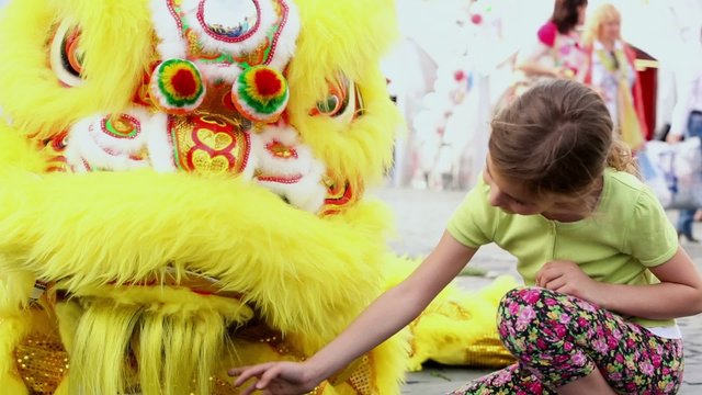People walk near young girl which plays with furry dragon 