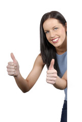 Attractive friendly female girl or woman smiling peeking looking round a plain white board or wall...