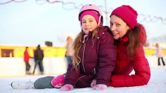 Happy mother and daughter sit at ice rink after skating