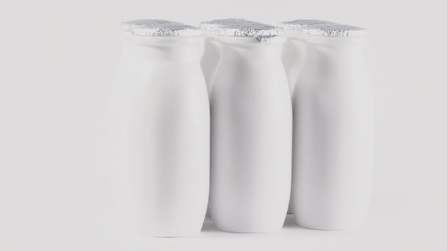 Six plastic bottles with foil cap of yogurt circling on table