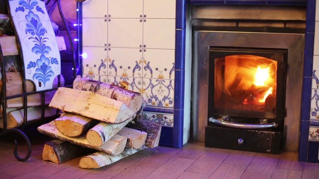 Fireplace with burning flame and stack of birch firewood.