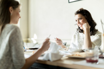 Two beautiful ladies eating in a restaurant while talking