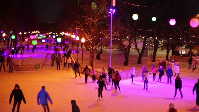 People are skating on evening rink with purple lights