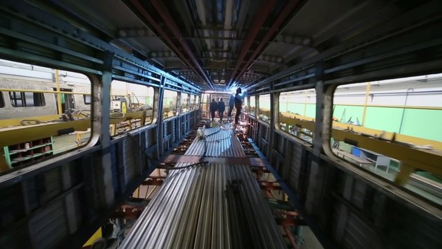Workers weld inside dark train coach at workshop in factory