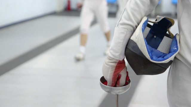 Fencer hold rapier and helmet, closeup view in sport club during training