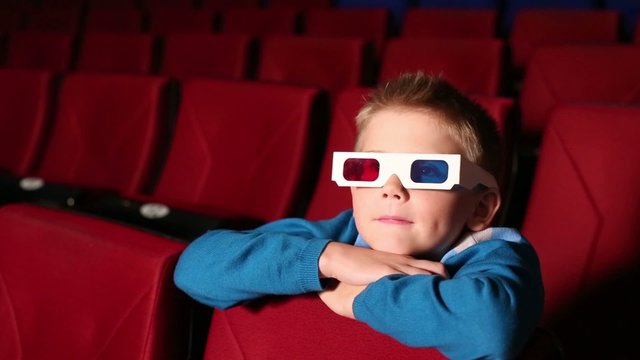Little boy in 3D glasses sits in cinema hall and watching movie