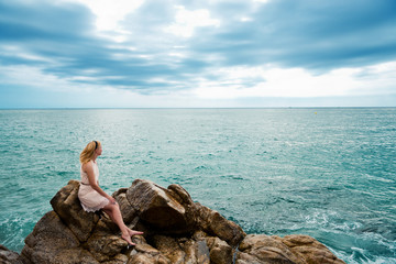 Fototapeta na wymiar Beautiful young woman sitting on the stone on the seashore