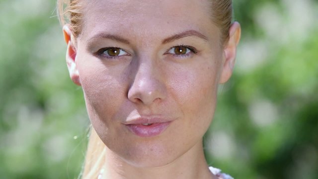 Young woman looks and smiles at sunny summer day, closeup