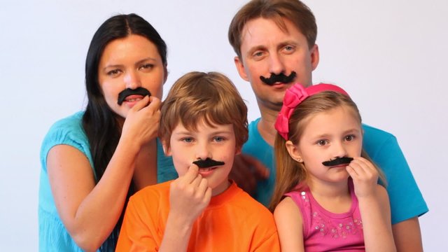 father, mother, daughter and son with false moustaches at all unstick them and hold on outstretched arms