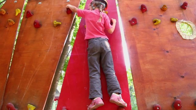Little girl crawls on pendant wall in outdoor climbing center